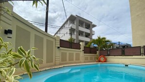 A swimming pool with a curved edge, surrounded by a low wall and potted plants. - The Monalysa Suites & Residence (Grand-Baie)