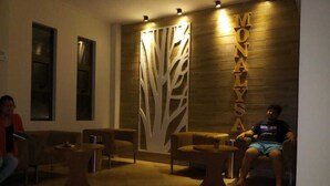 A reception area with a wooden wall, a decorative tree design, and two seating areas with tables. - The Monalysa Suites & Residence (Grand-Baie)