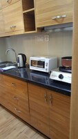 A kitchen with wooden cabinets, a microwave, a kettle, and a stove.