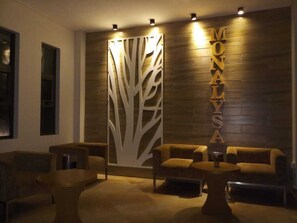 A reception area with a wooden wall, a decorative tree panel, and the name 'MONALYSA' in gold letters. There are two sofas and a round coffee table. - The Monalysa Suites & Residence (Grand-Baie)