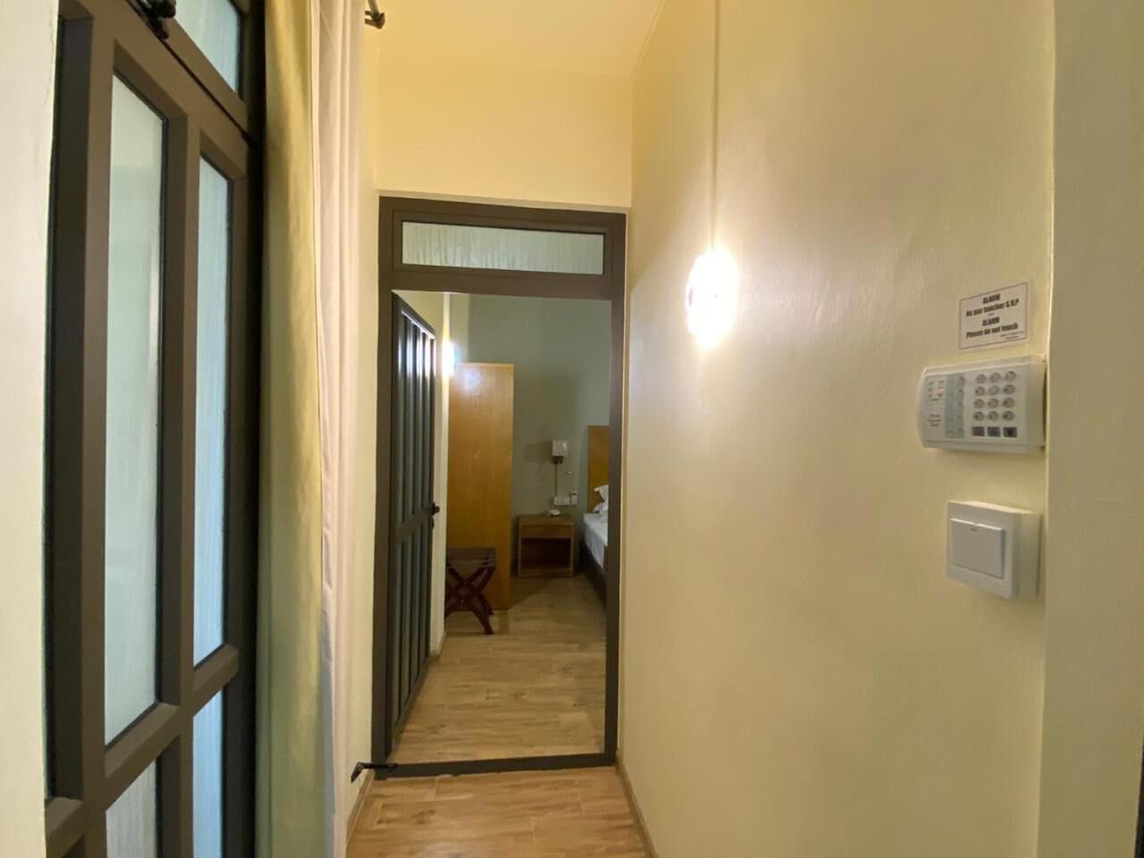 Um corredor estreito com piso de madeira que leva a um quarto com cama e mesa de cabeceira.
