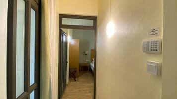 Um corredor estreito com piso de madeira que leva a um quarto com cama e mesa de cabeceira.