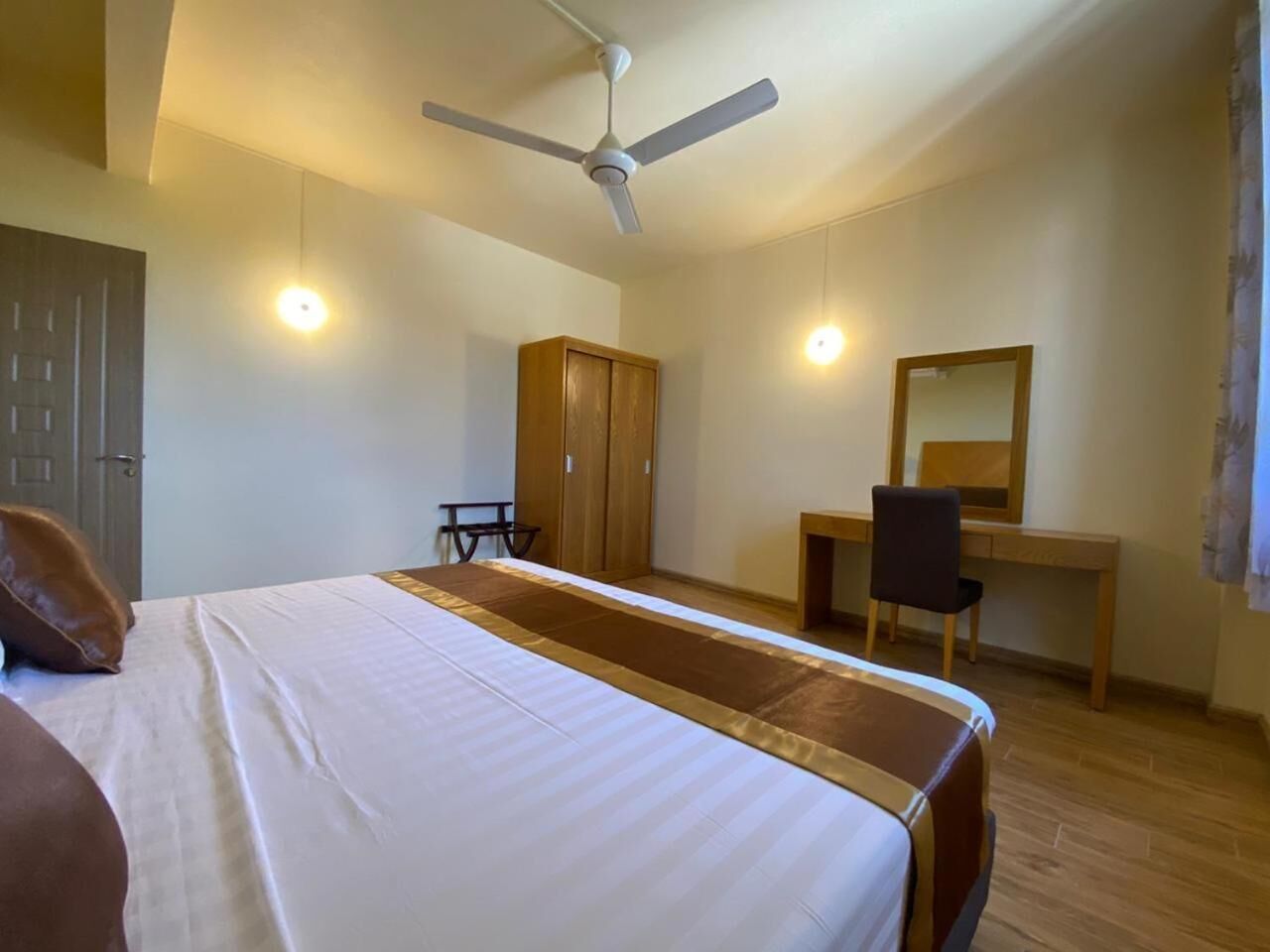 A bedroom with a bed, a desk, a chair, a wardrobe, and a ceiling fan.