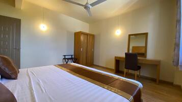 A bedroom with a bed, a desk, a chair, a wardrobe, and a ceiling fan.