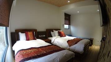 Habitación de hotel con dos camas, cada una con cabecero de madera y ropa de cama blanca. Se ve una ventana en un lateral y una pared de madera en el otro.