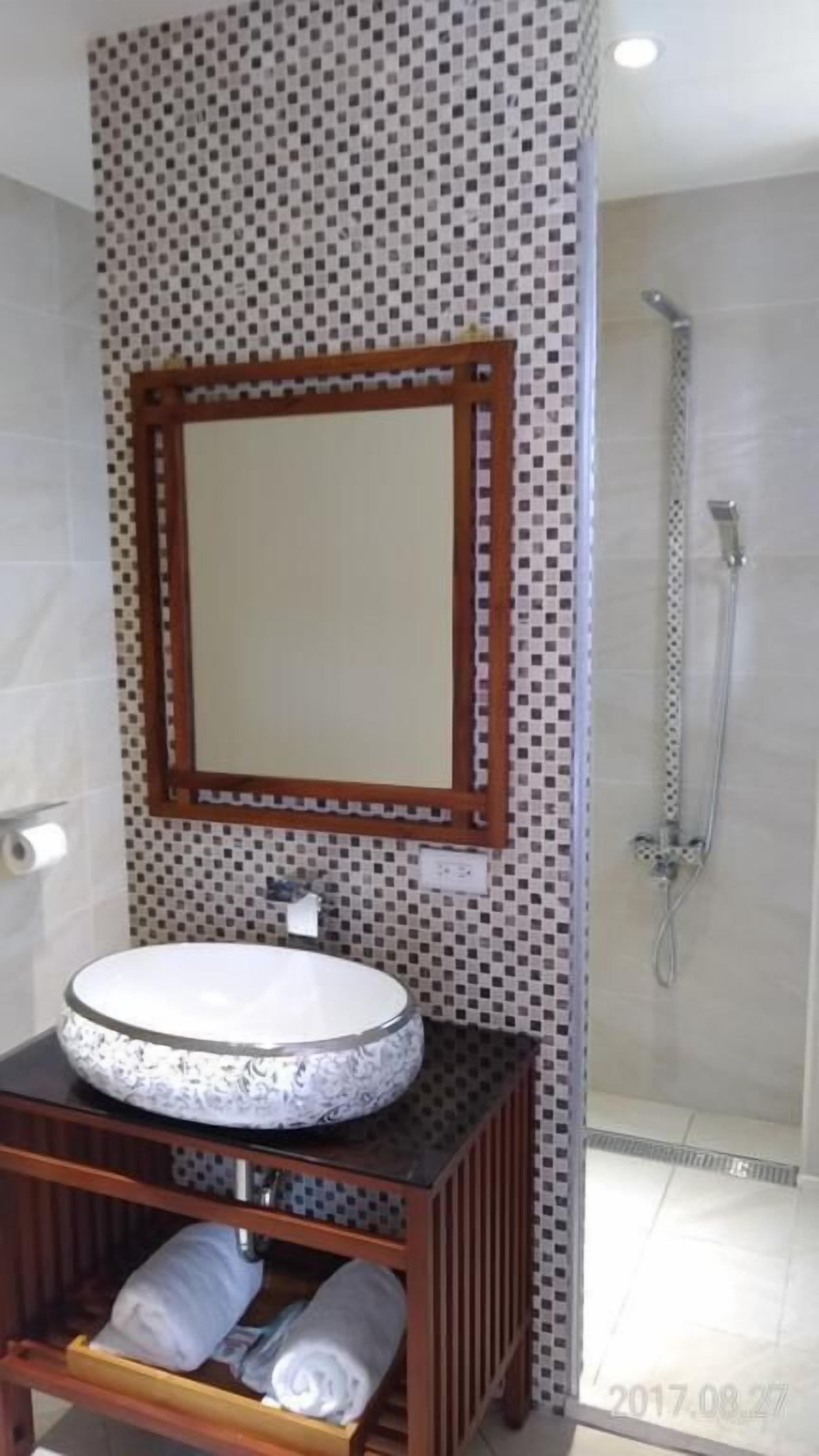 Un baño con un lavabo redondo, un espejo con marco de madera, una ducha y una pared con azulejos.