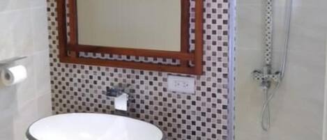 Un baño con un lavabo redondo, un espejo con marco de madera, una ducha y una pared con azulejos.