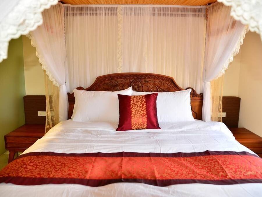 Una cama con dosel, ropa de cama blanca y una almohada decorativa roja y dorada.