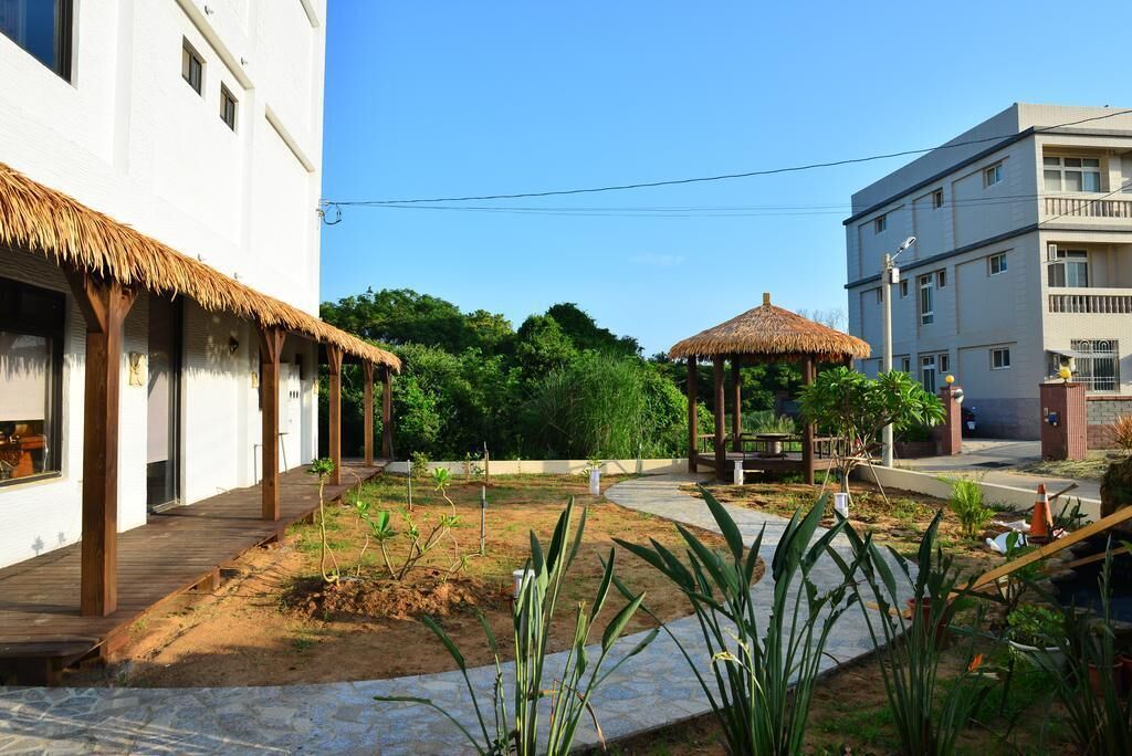 Un patio con cubierta de madera, un pabellón de techo de paja y un edificio blanco con balcón.