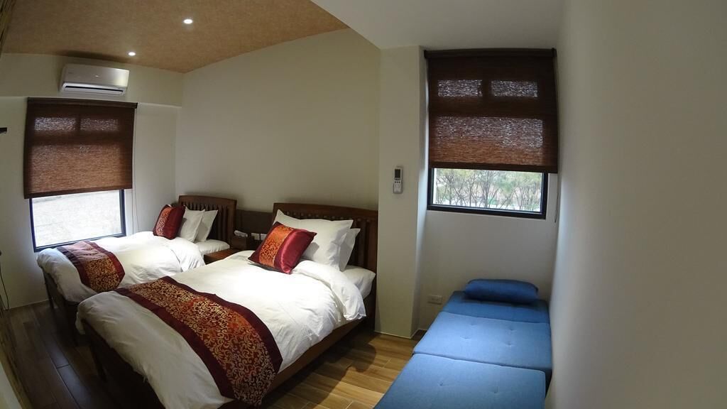 A hotel room with two beds, a bench, and a window with blinds.