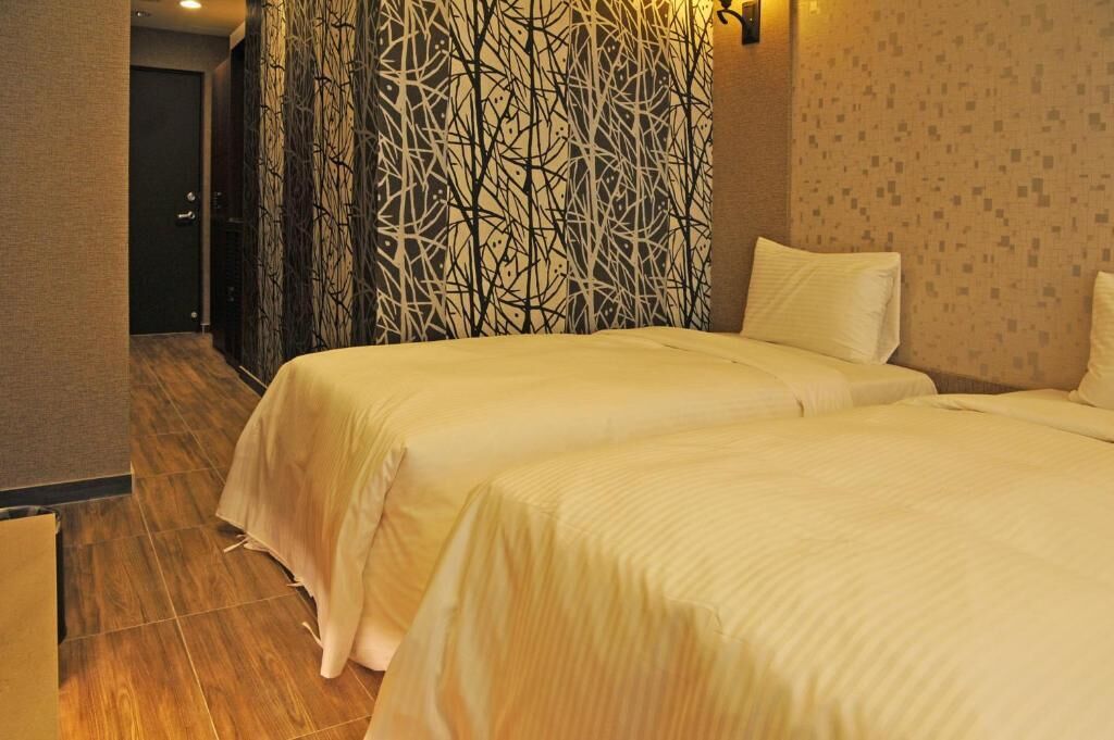A hotel room with two beds, a patterned curtain, and a tiled floor.