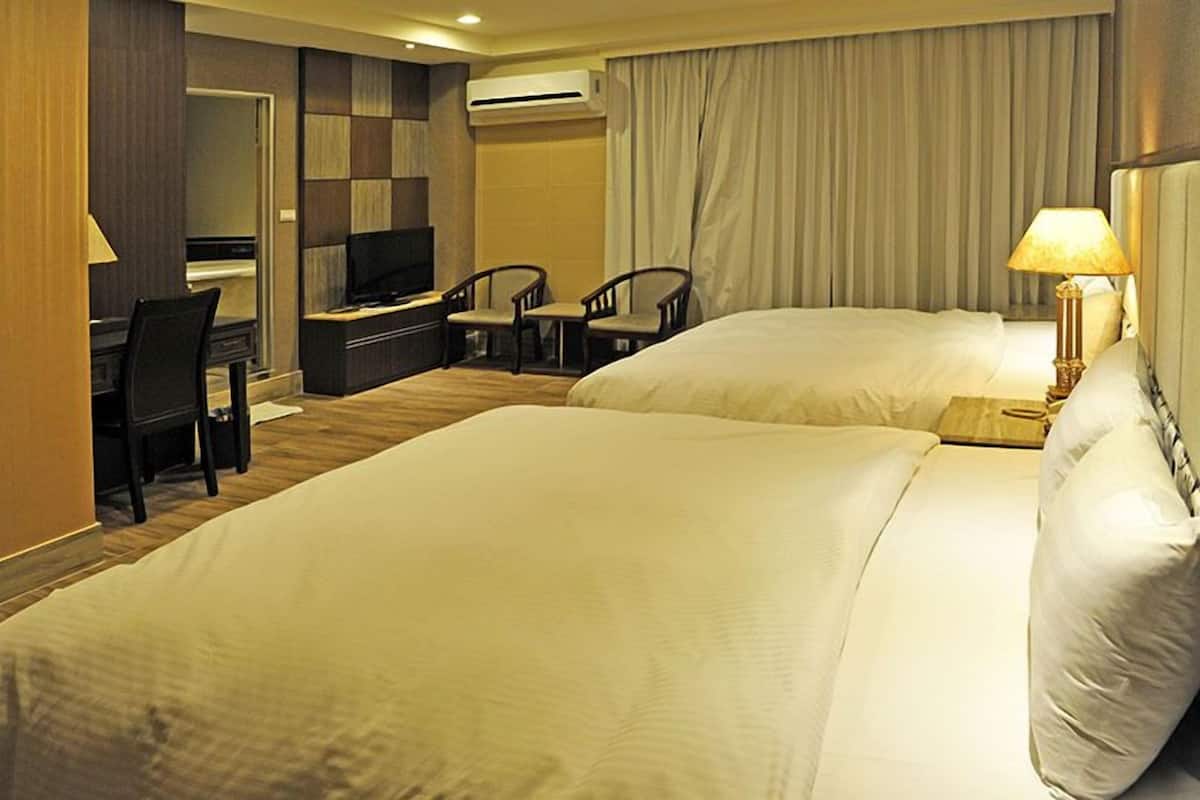 A hotel room with two beds, a desk with a TV, and two chairs.