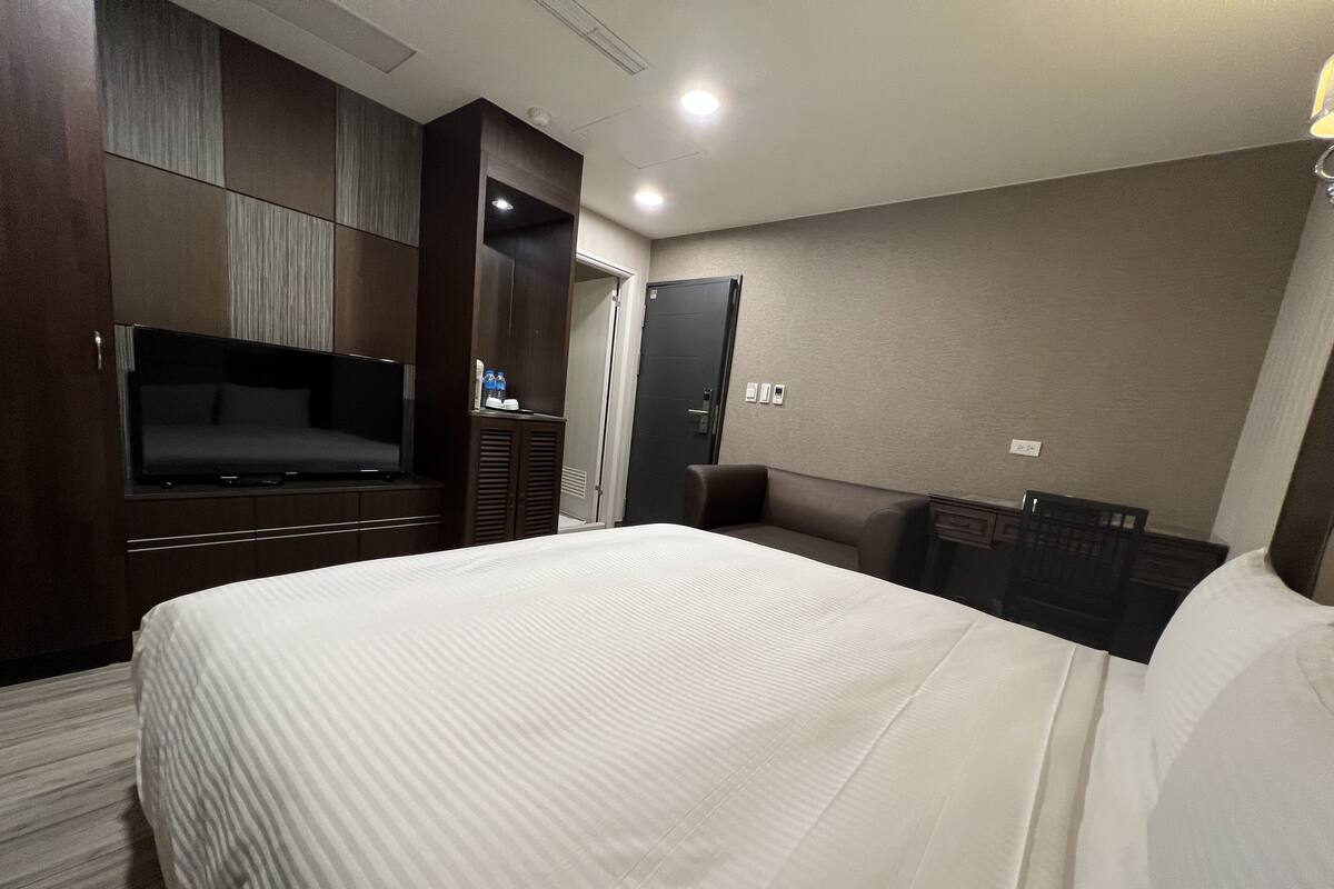 A hotel room with a large bed, a flat-screen TV, a wardrobe, and a desk with a chair.