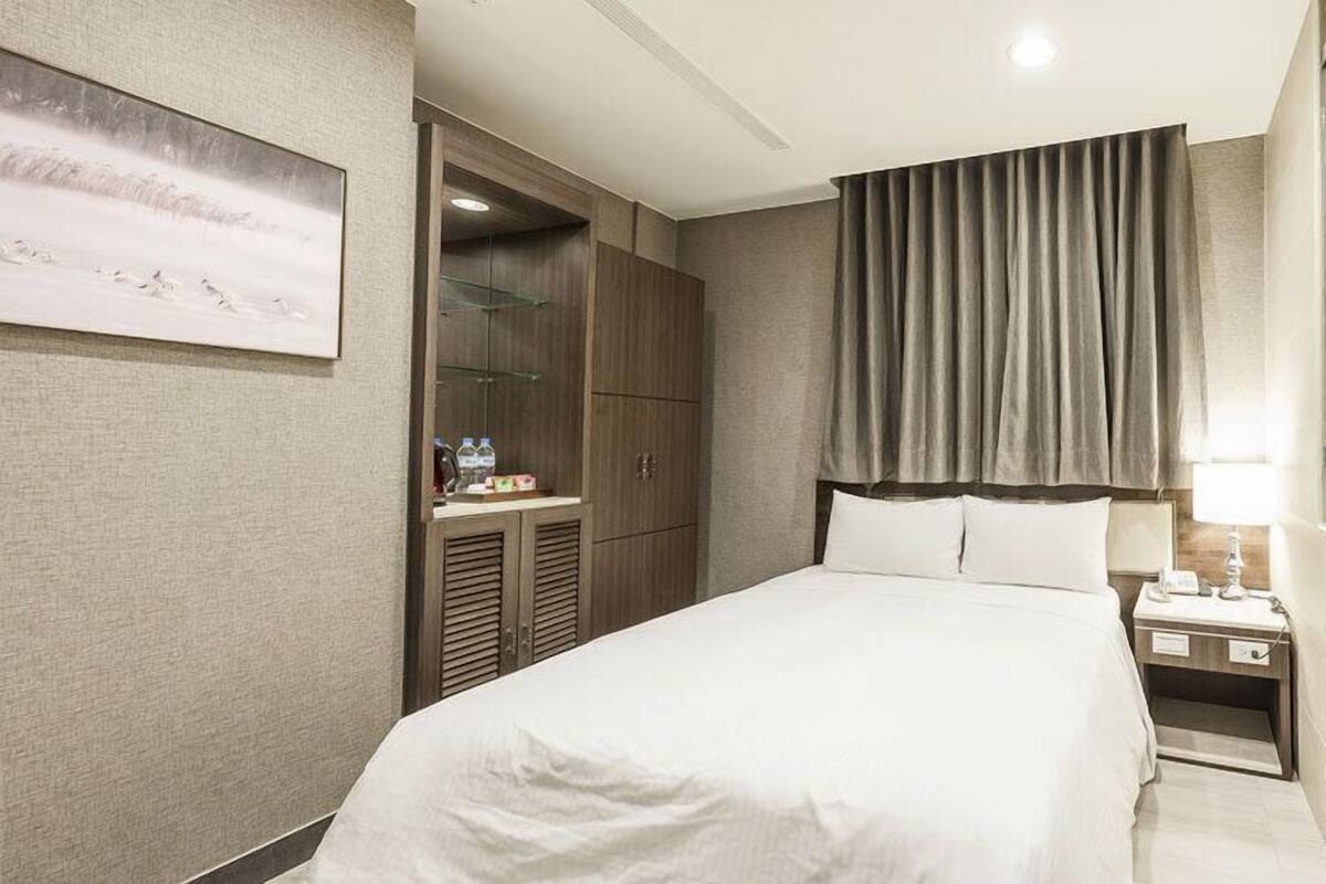 A hotel room with a large bed, a nightstand, a wardrobe, and a painting on the wall.