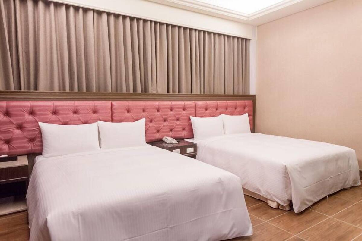 A hotel room with two beds, a wooden nightstand, a telephone, and a window with curtains.
