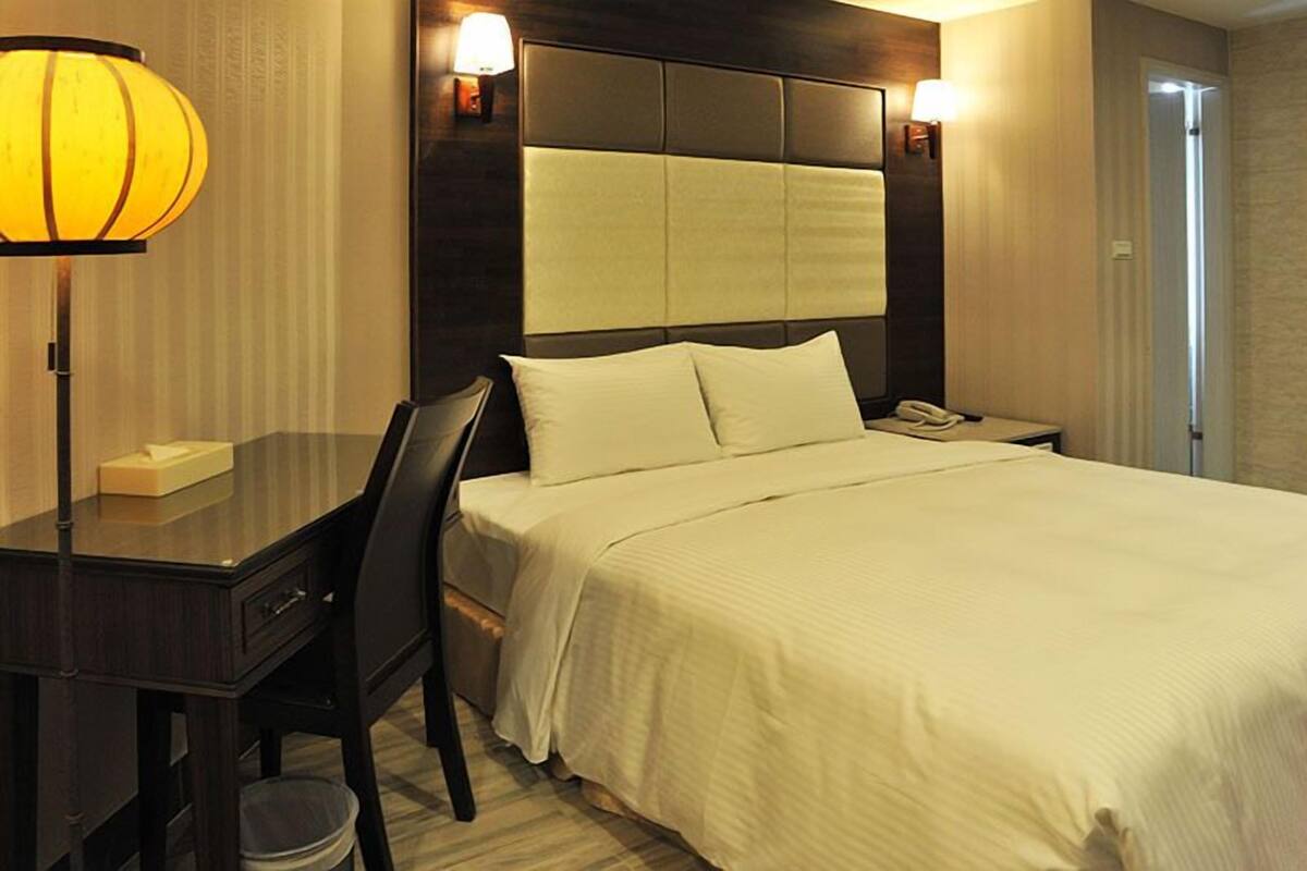 A hotel room with a bed, bedside table, lamp, and a chair.