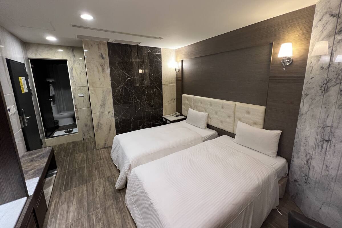 A hotel room with two beds, a shower area, marble walls, and a wooden floor.