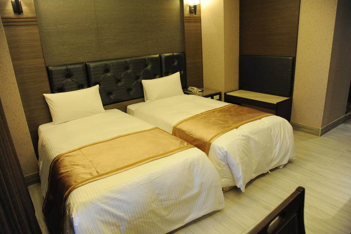 A hotel room with two beds, a nightstand, a TV, and a small table.