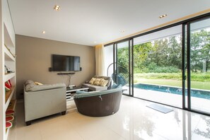 A modern living room with a grey sofa, a large wicker chair, and a flat-screen TV mounted on the wall. - The Point Villa (Da Nang)