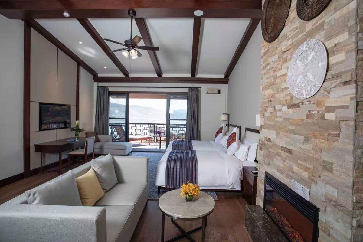 Une chambre d’hôtel avec un lit, un canapé, une table à manger et un téléviseur. Elle dispose d’un balcon avec vue sur l’océan.