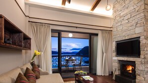 Een gezellige woonkamer met een bank, salontafel en open haard. Achter de glazen deuren is een balkon met een tafel en stoelen te zien.