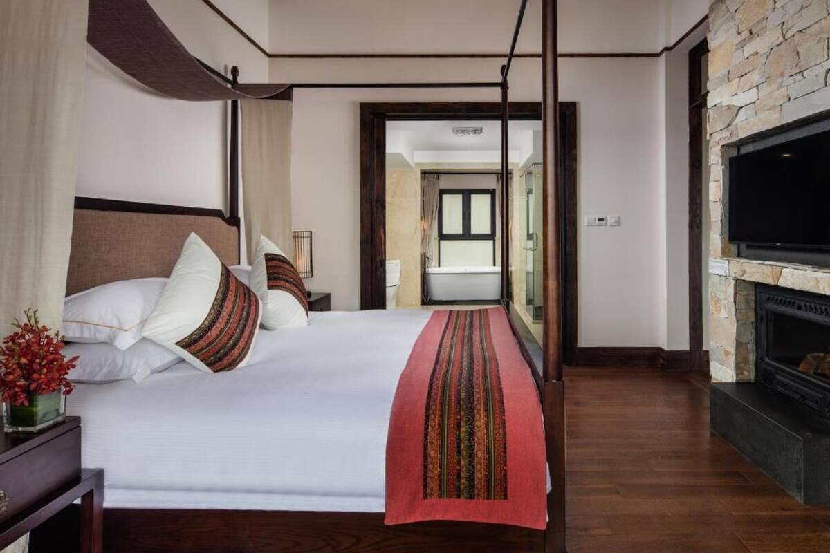 Une chambre à coucher avec un grand lit, une cheminée en pierre et une vue sur la salle de bain par une porte ouverte.