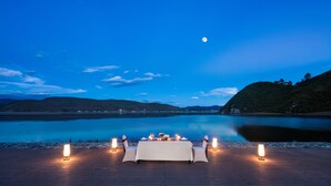 Een tafel voor twee met kaarsen op een houten terras, uitkijkend over een rustig meer 's nachts.