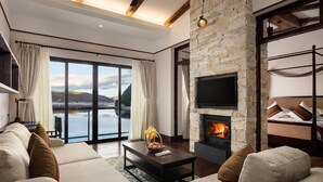 Een moderne woonkamer met een stenen open haard, grote ramen en uitzicht op de natuur.
