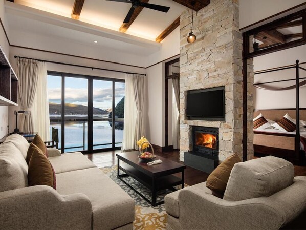 A modern living room with a stone fireplace, large windows, and a view of the outdoors. - High Mountain Resort Shangri-la (Deqin)