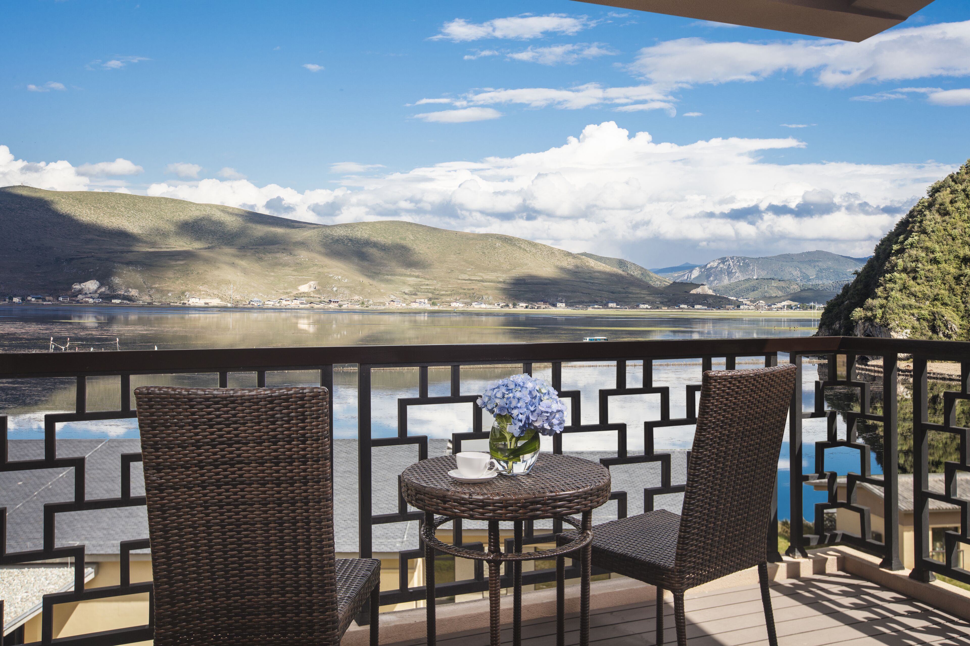 Un balcone con sedie in vimini e un tavolo, con vista su un lago e montagne.