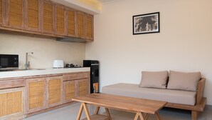 Une cuisine moderne avec des meubles en bois, un plan de travail blanc, une machine à café et un canapé beige dans l’espace salon.