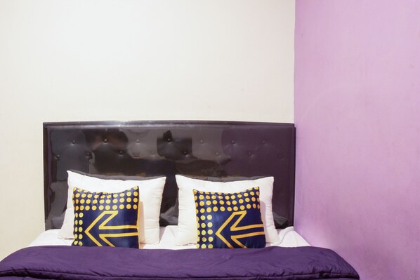 A bed with a dark headboard, two pillows with a geometric pattern, and a purple blanket. - Ungu Residence Syariah (Bandung)
