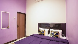 A bedroom with a purple wall, a wooden door, a bed with a black headboard, and patterned pillows. - Ungu Residence Syariah (Bandung)
