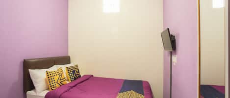 A bedroom with a bed, pillows, a blanket, an air conditioner, a mirror, and a television.