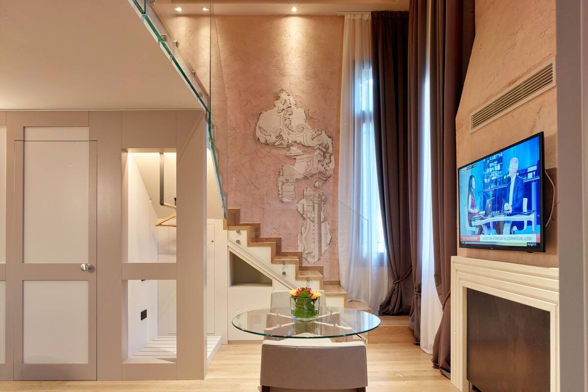 Ein modernes Wohnzimmer mit Glastisch, Wanddeko, Fernseher und einer Treppe.