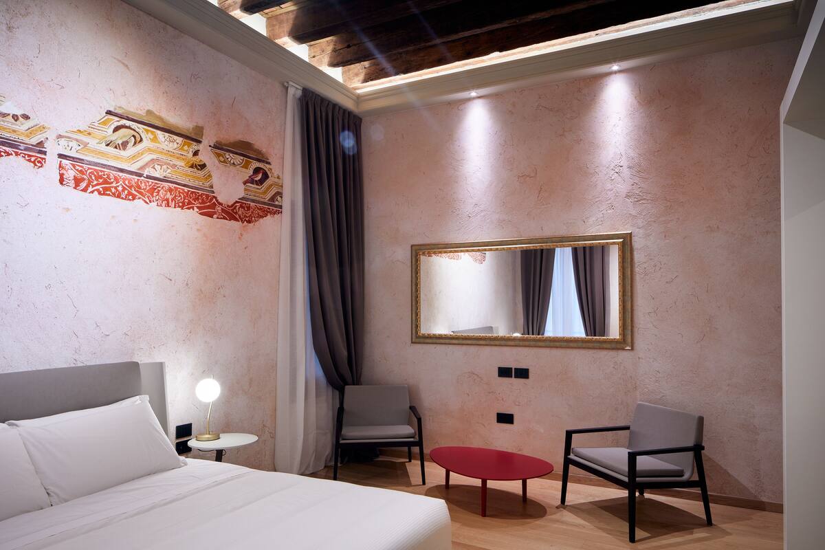 Ein Hotelzimmer mit einem Bett, zwei Stühlen, einem kleinen Tisch, einem Spiegel und einer Wand mit dekorativer Verkleidung.