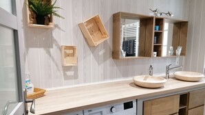 Een moderne badkamer met een houten wastafel, twee wasbakken, een spiegel, een plant en een ingebouwde wasmachine.
