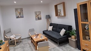 Een moderne woonkamer met een grijze bank, twee fauteuils, een houten salontafel en een kast met glazen deuren.