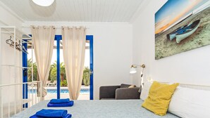 Een slaapkamer met een bed, een bureau, een stoel, een raam met gordijnen en uitzicht op een zwembad en strand.