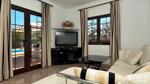 A modern living room with a sofa, a TV, and a pool view. - Villa Timanfaya Private Pool By PVL (Yaiza)