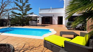 A swimming pool with a patio area, outdoor furniture, and a white building in the background. - Villa Timanfaya Private Pool By PVL (Yaiza)