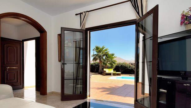 A modern room with a glass door leading to a pool area, a bed, and a TV. - Villa Timanfaya Private Pool By PVL (Yaiza)