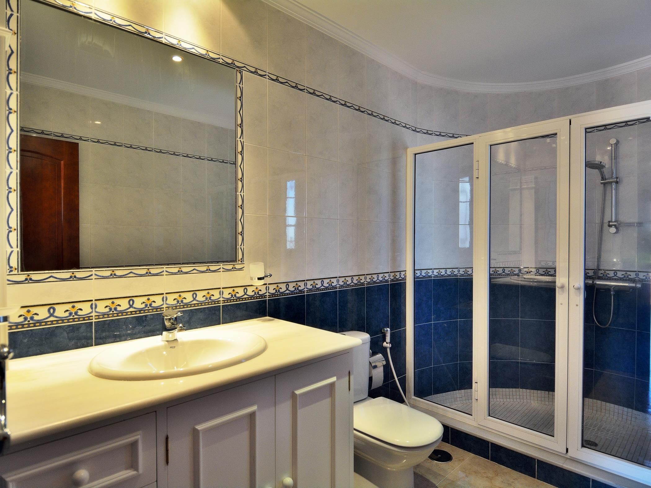 Een badkamer met een wit wastafelmeubel, toilet en douche met glazen deur.