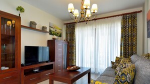 A living room with a TV, wooden cabinet, sofa, and patterned curtains.