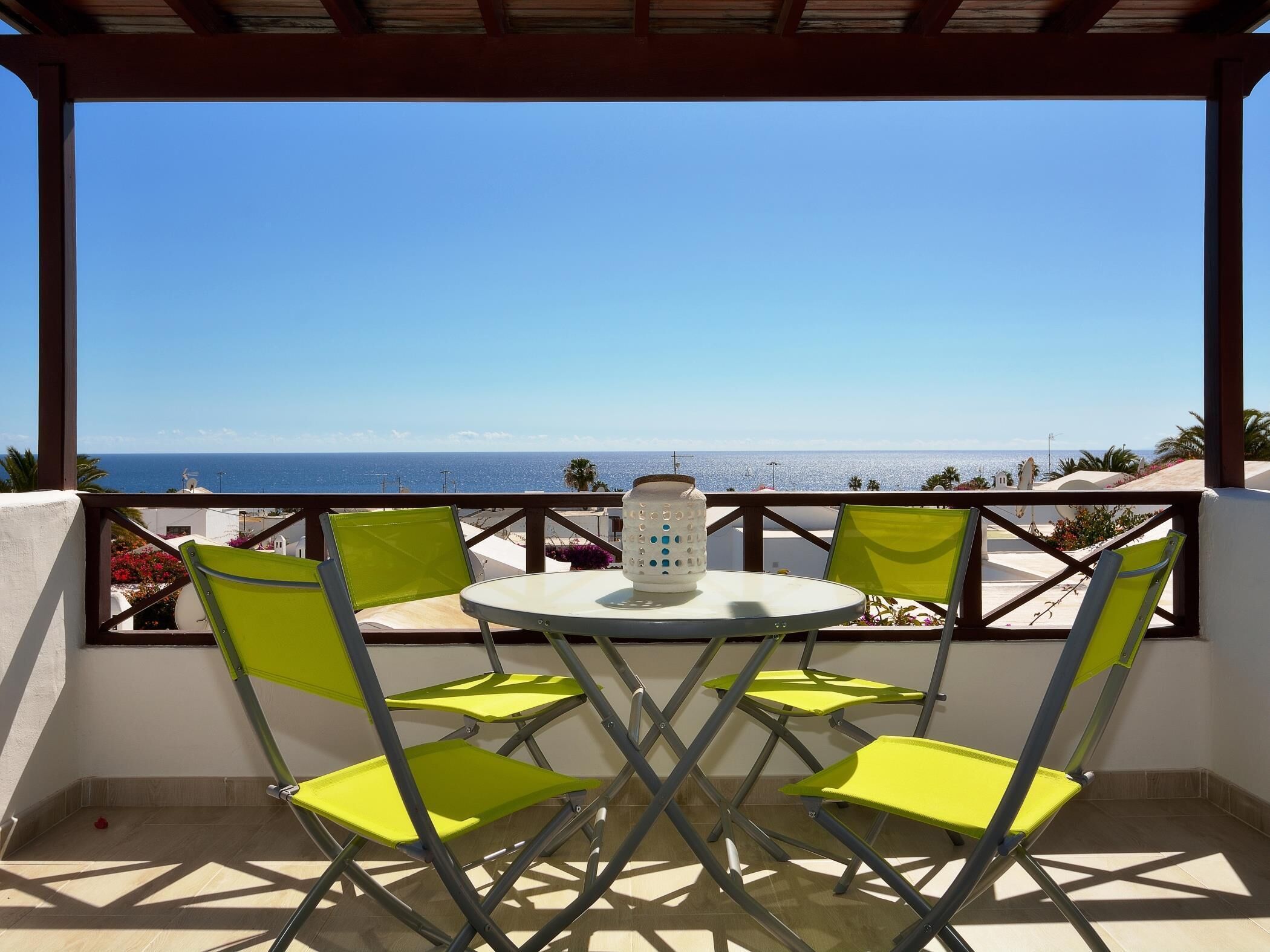 A balcony with a table and chairs, overlooking a coastal view.