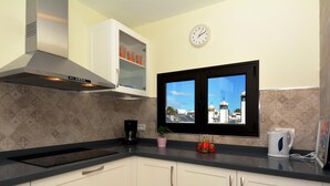 A modern kitchen with white cabinets, a stainless steel range hood, a coffee maker, and a window with a view of buildings.