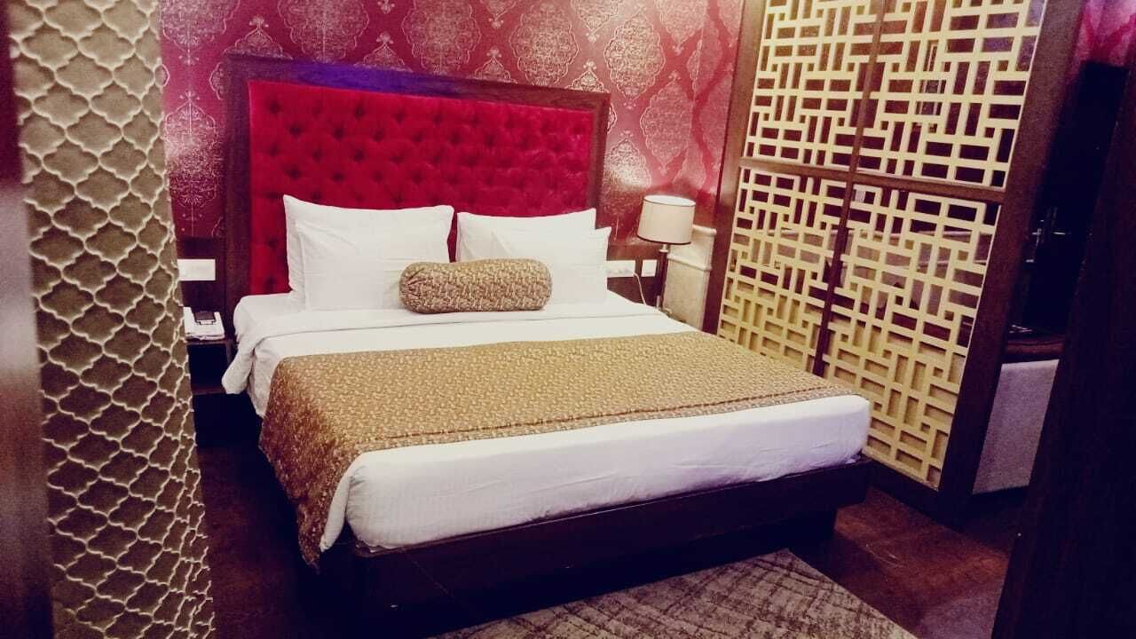 Habitación de hotel con una cama grande, cabecera roja, pared estampada y biombo decorativo.