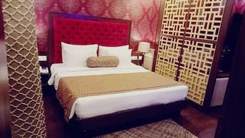 Habitación de hotel con una cama grande, cabecera roja, pared estampada y biombo decorativo.
