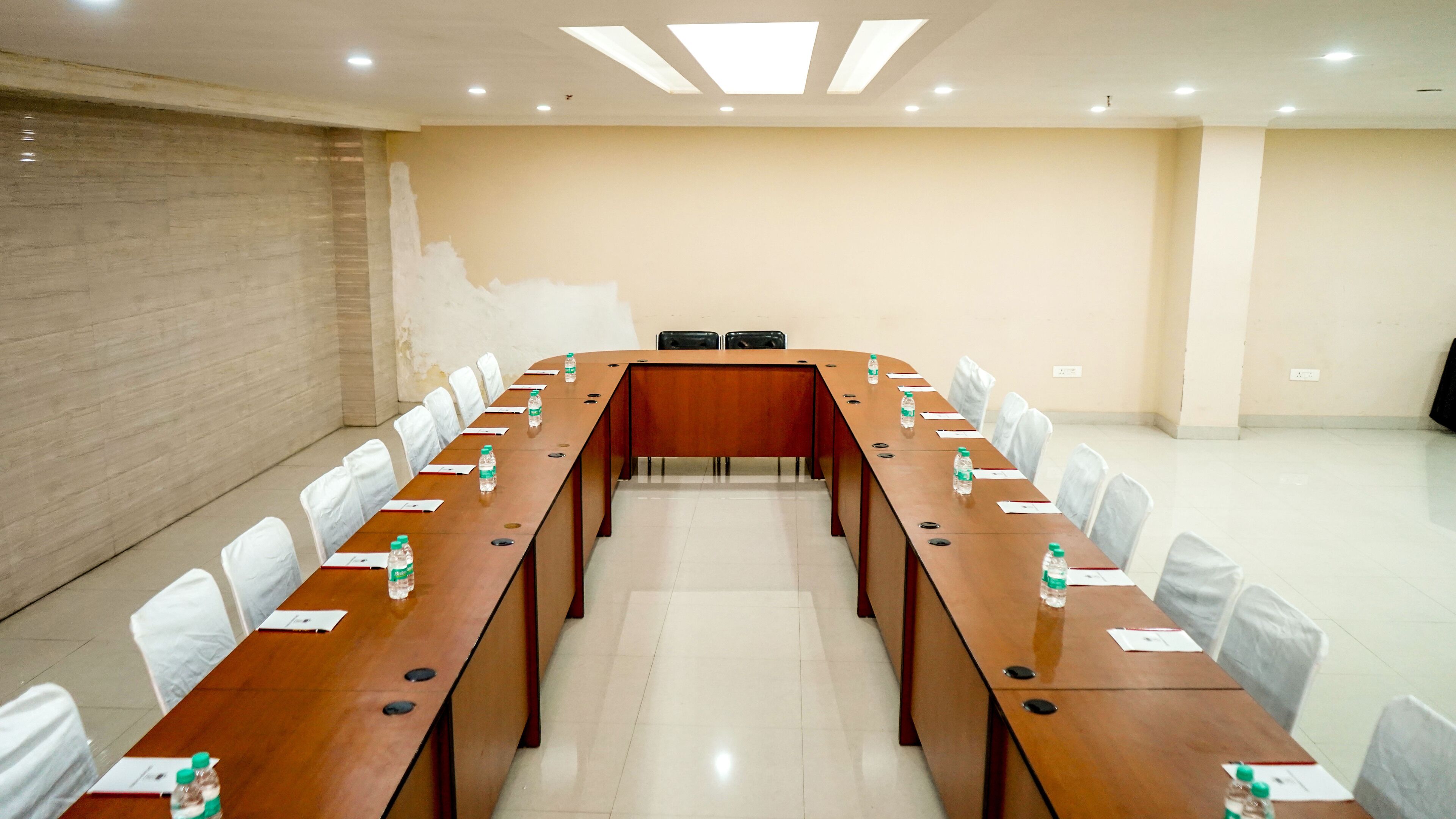 Un salón de conferencias con una larga mesa de madera, sillas blancas y botellas de agua sobre la mesa.