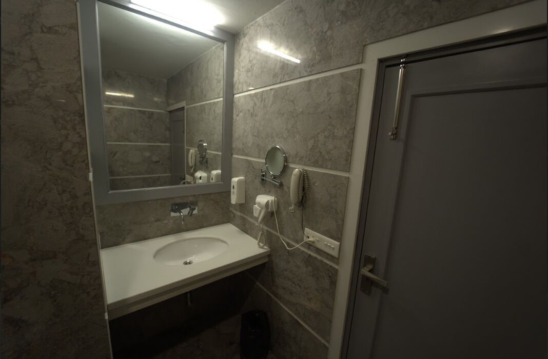 Une salle de bain avec un lavabo en marbre, un miroir, un distributeur de serviettes et un porte-rouleau de papier toilette.